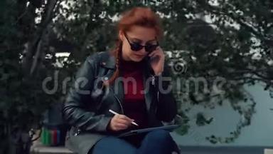 戴墨镜的年轻女子<strong>坐在公园里</strong>的长凳上，一边用手机说话，一边记录着在<strong>公园里</strong>的谈话